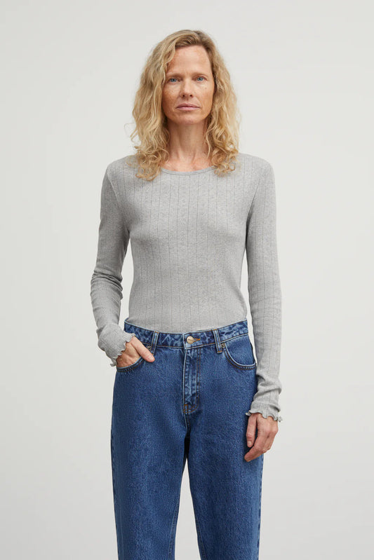 Woman wearing a gray sweater and blue jeans against a plain background