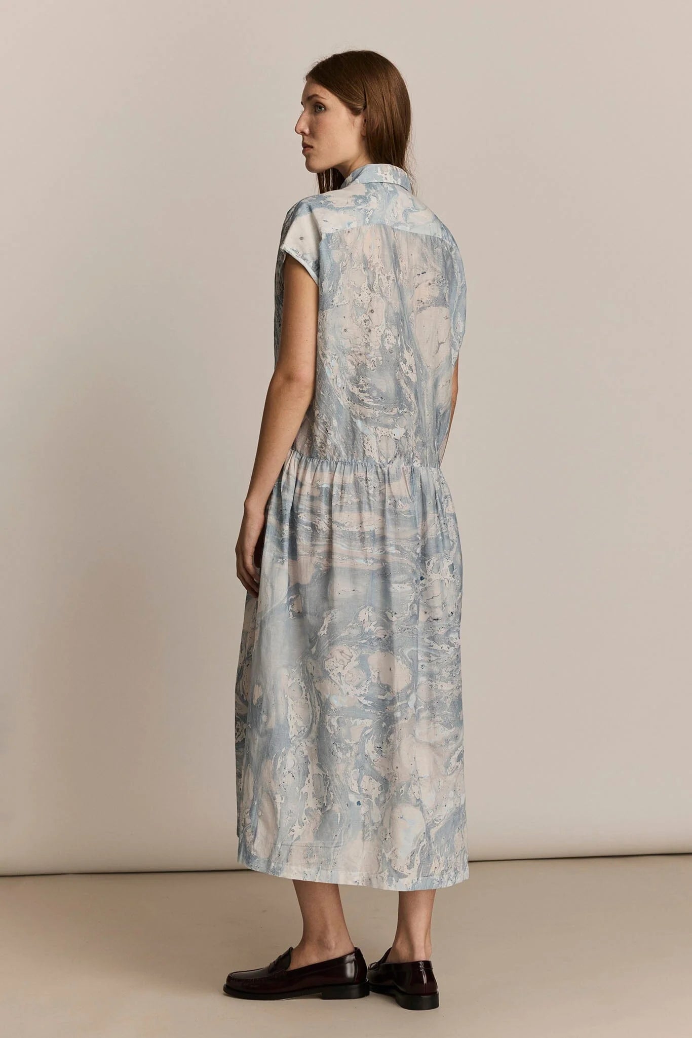 Woman wearing a light blue patterned dress on a beige background. Back view