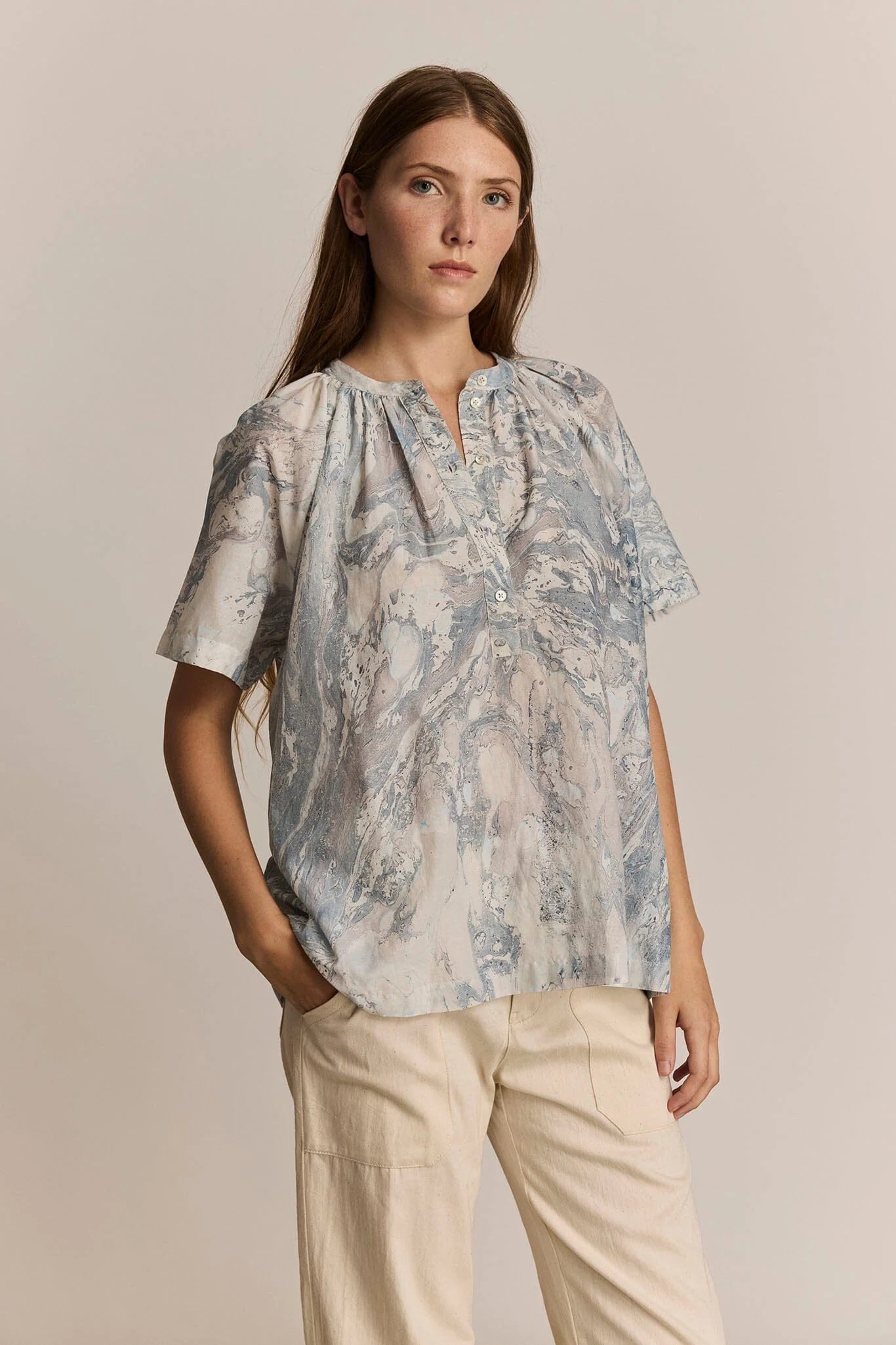 Woman wearing a print blouse and beige pants against a neutral background