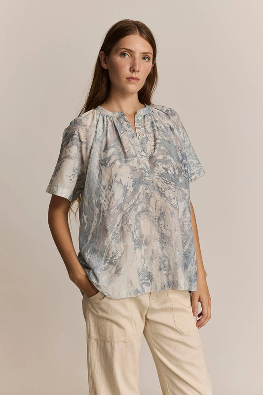 Woman wearing a print blouse and beige pants against a neutral background