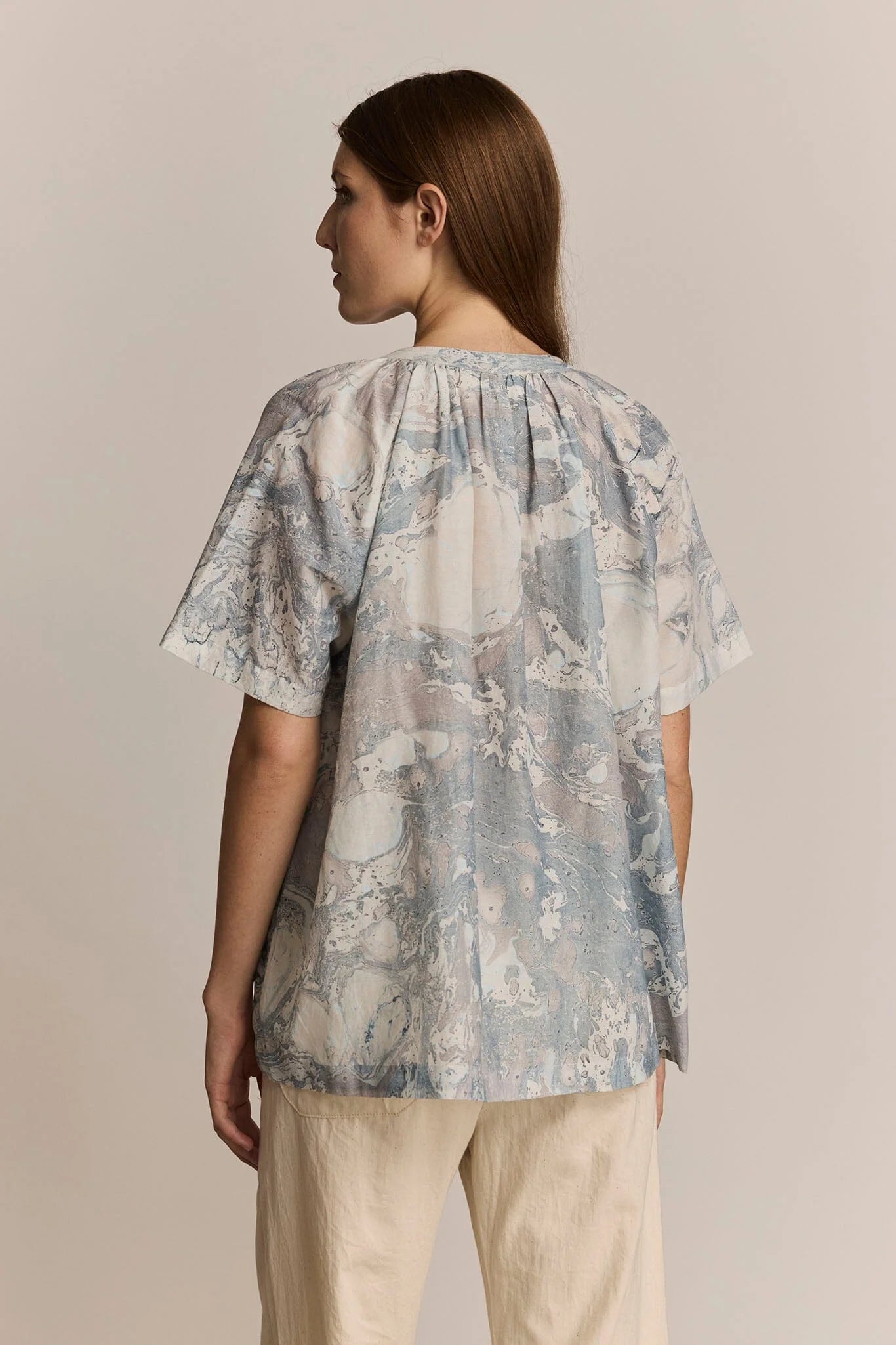 Woman wearing a patterned blouse against a plain background. Back view