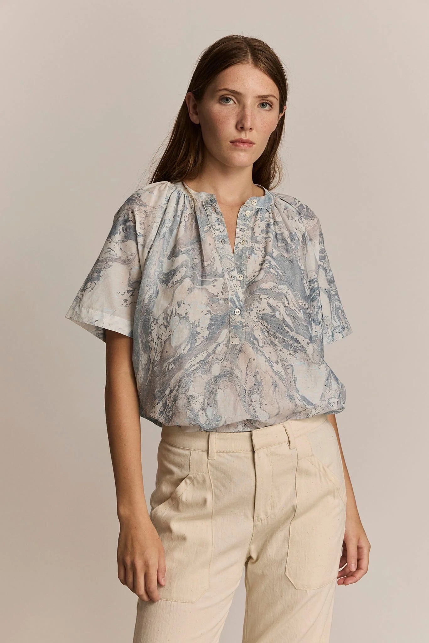 Woman wearing a patterned blouse and beige pants against a plain background. Front button closure