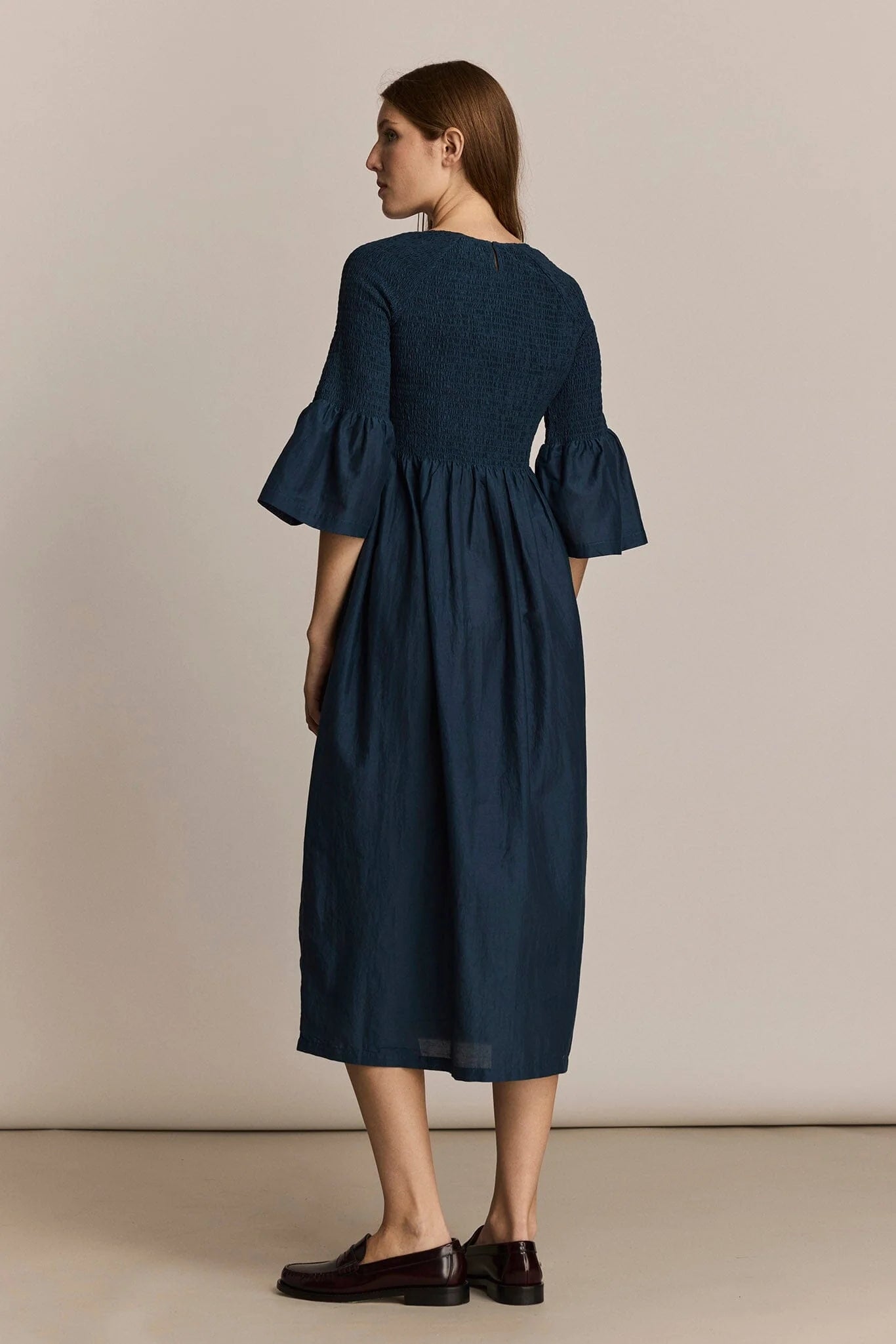 Woman wearing a dark blue dress with bell sleeves against a beige background