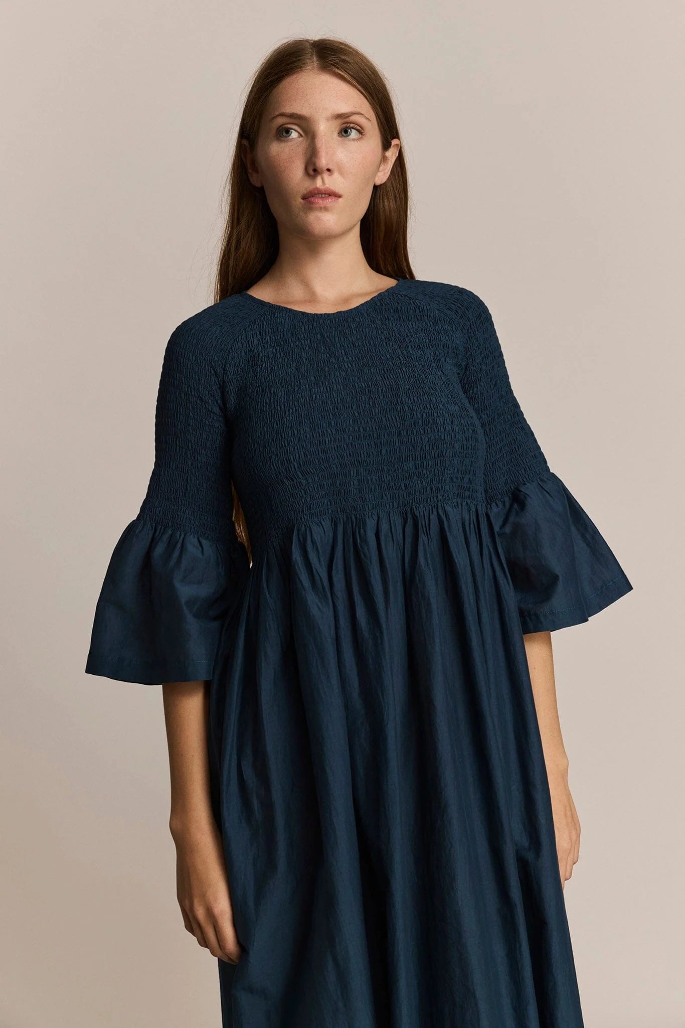 Woman wearing a dark blue dress with ruffled sleeves against a beige background