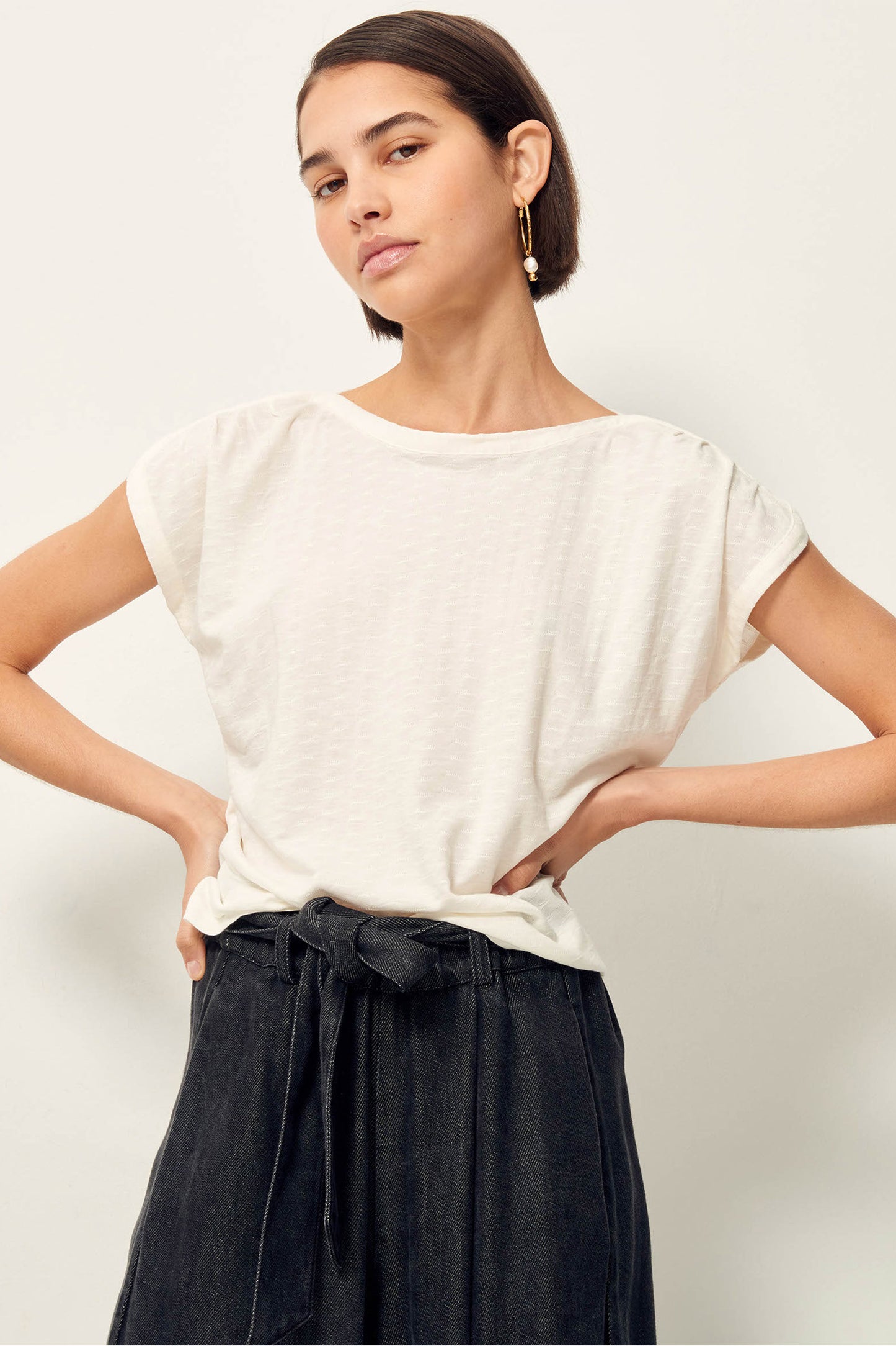 3/4 length picture of young women with short dark brown hair and brown eyes wearing white tee shirt with dark grey skirt.