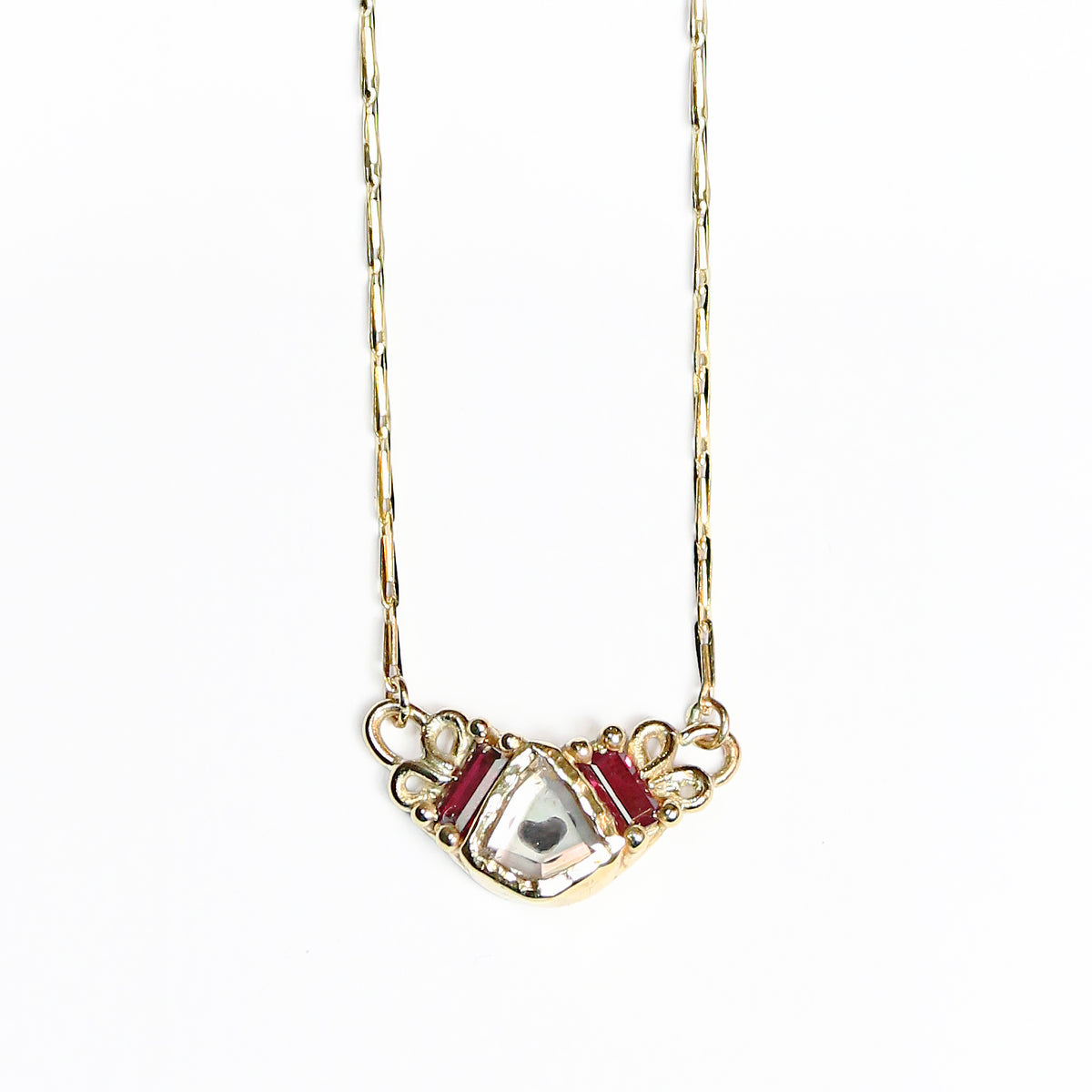 A yellow gold necklace with hidden heart shown behind a stunning white sapphire, and surrounded by a pair of rubies.