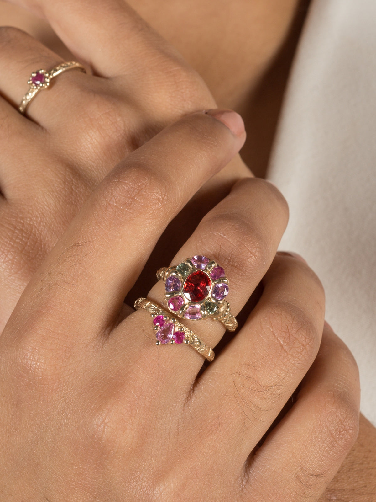 A model hand shown wearing three yellow gold rings with mutli-colored gemstones.
