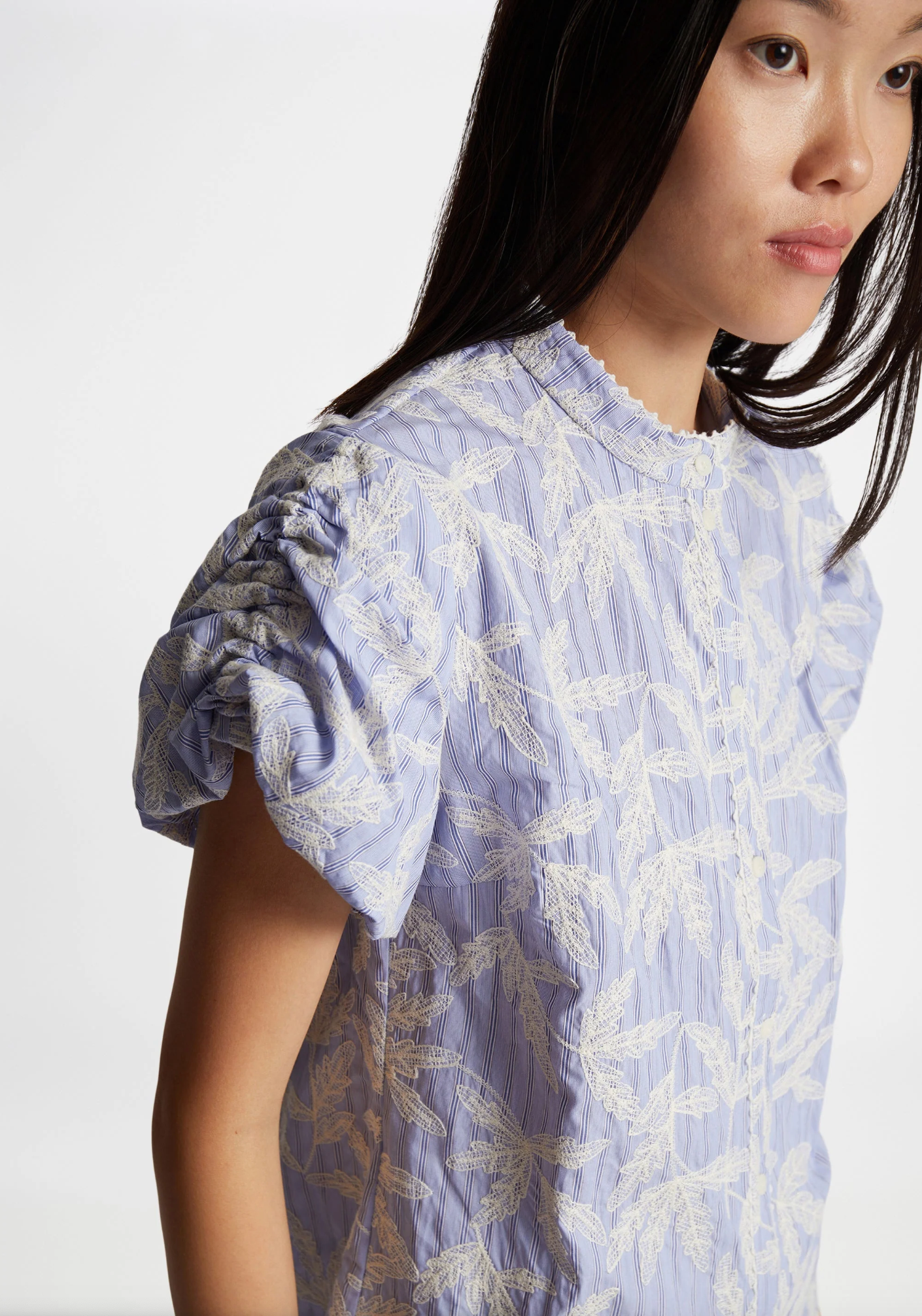 Woman with long black hair wearing pale blue short puff sleeve blouse with white leaf motif embroidery