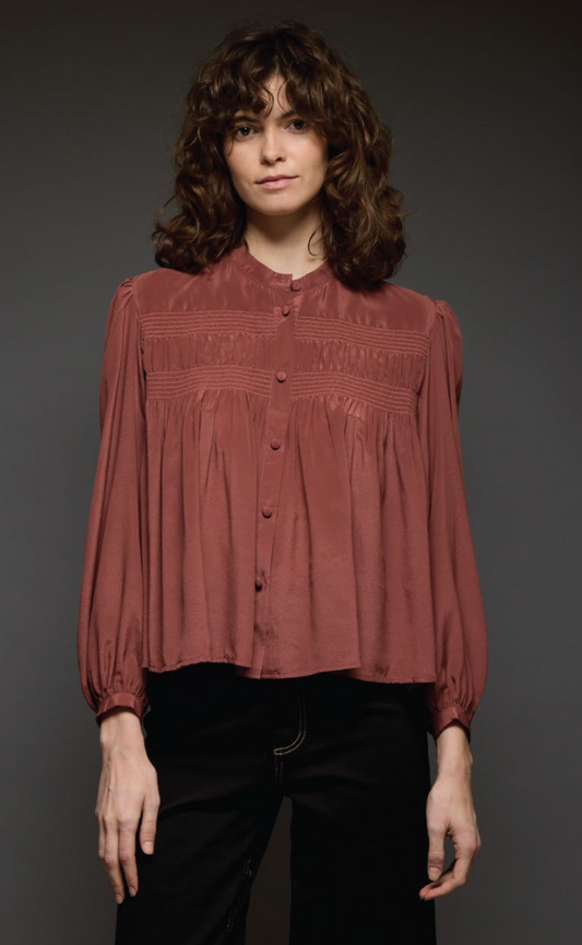Woman wearing a rust-colored blouse against a dark background