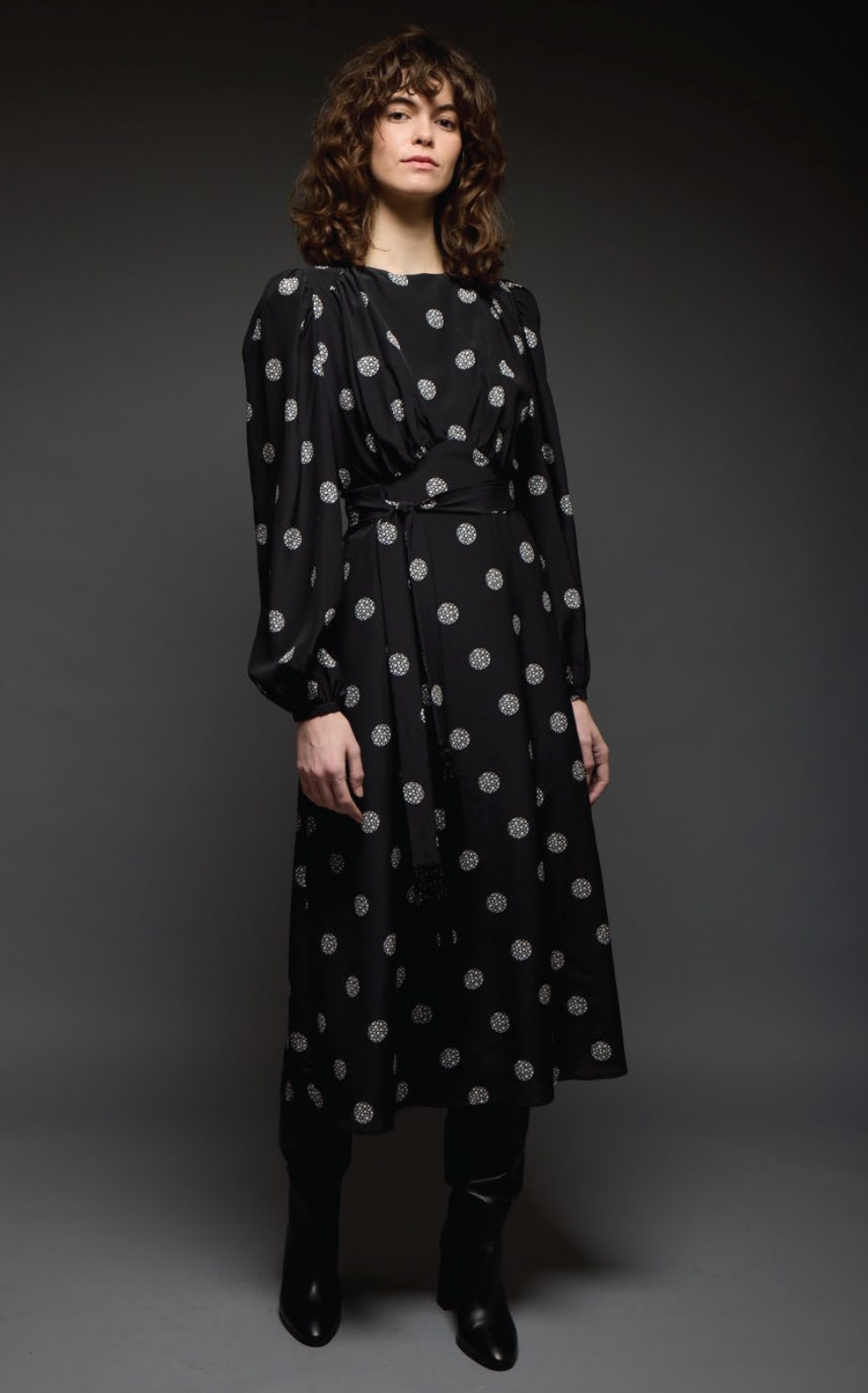 Woman wearing a black dress with white polka dots against a dark background