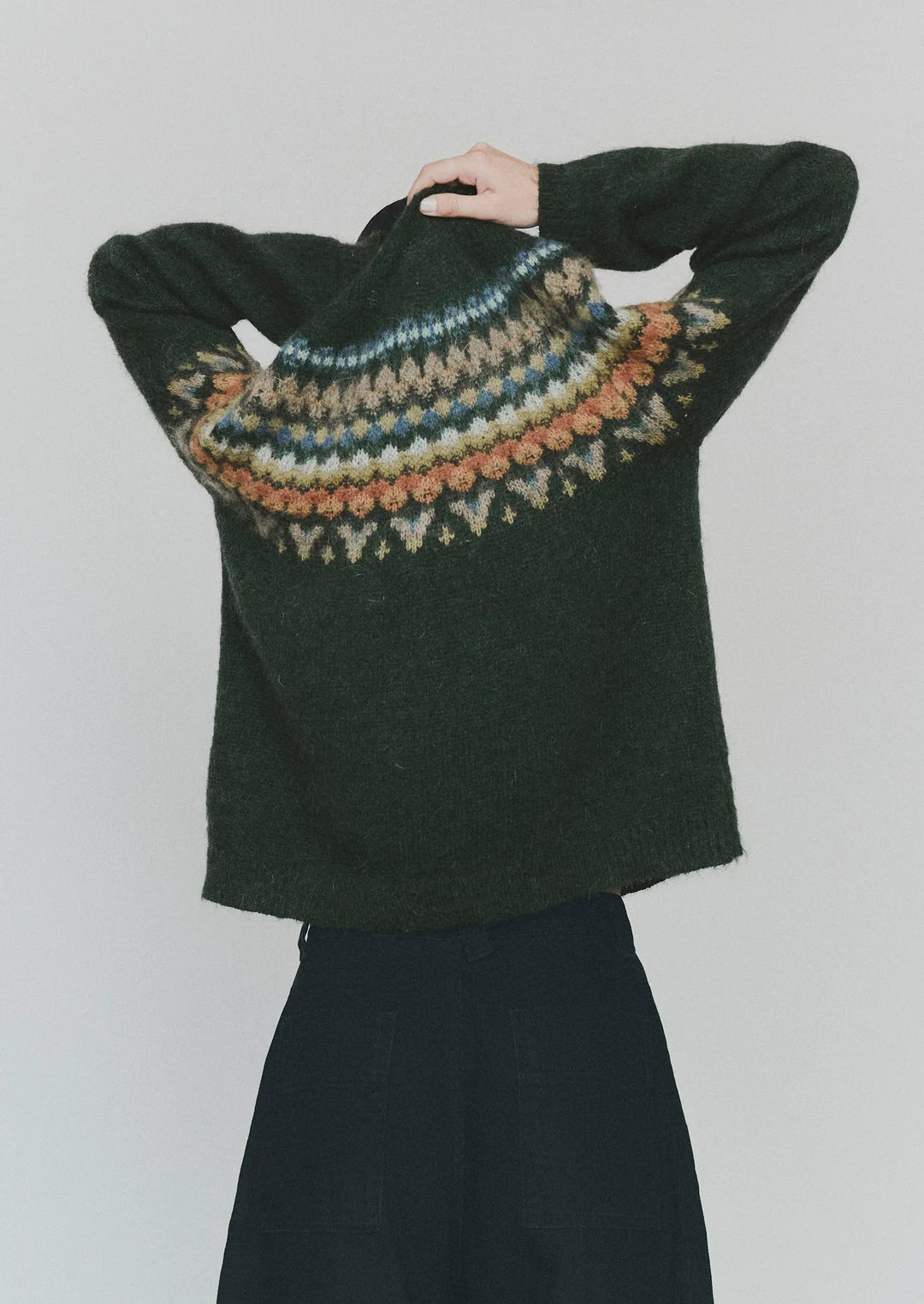 Dark green sweater with a colorful pattern on the back against a plain background