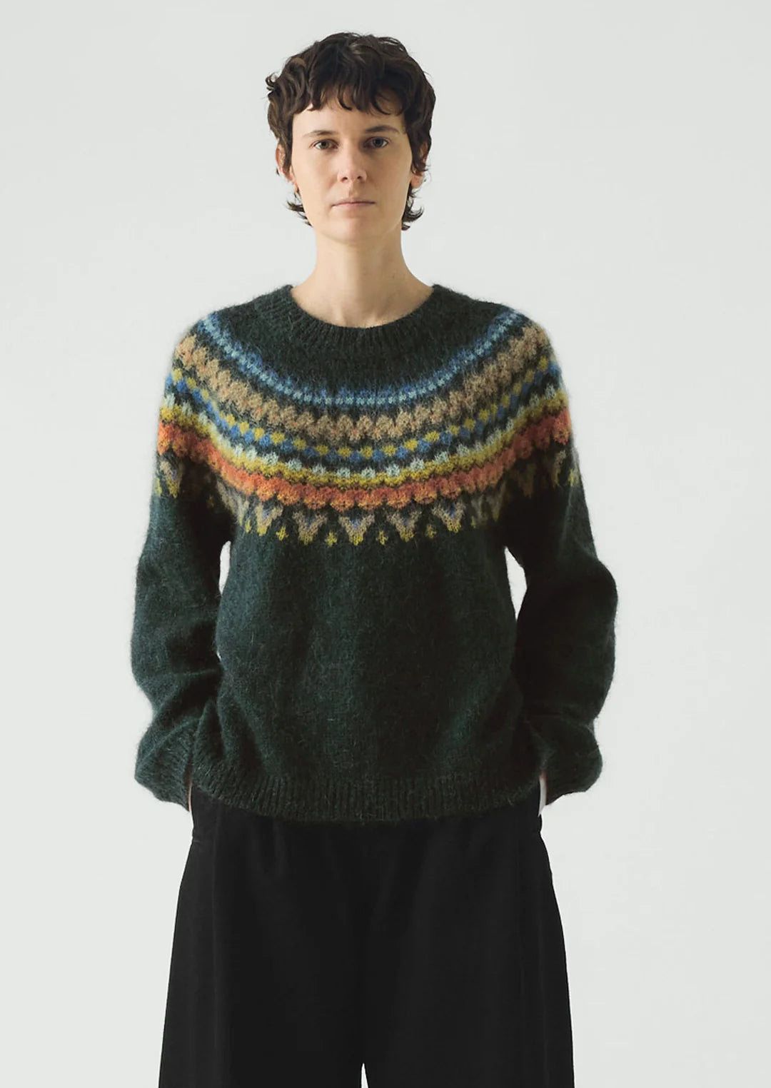 Person wearing a dark green sweater with colorful pattern on a white background