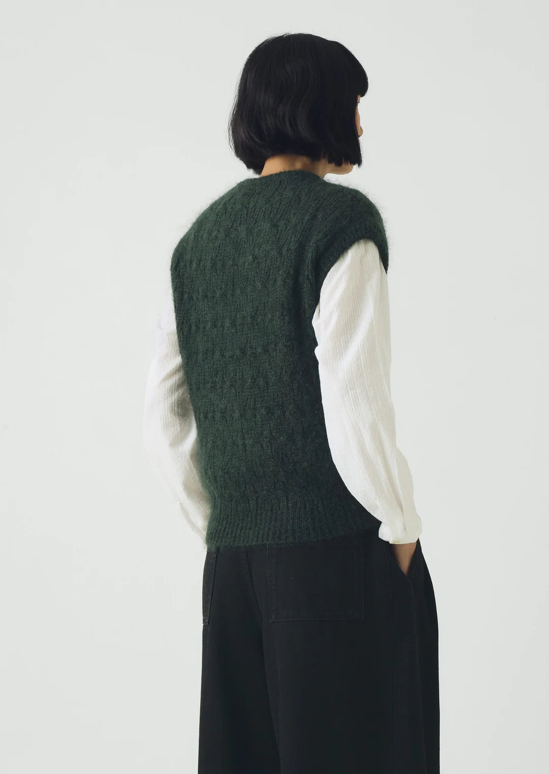 Person wearing a green knitted vest over a white shirt with a plain background