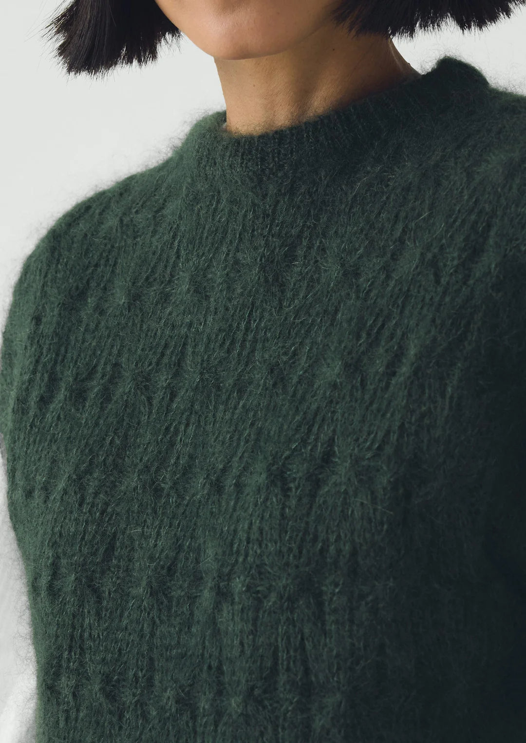 Close-up of a person wearing a dark green knitted sweater with a blurred background