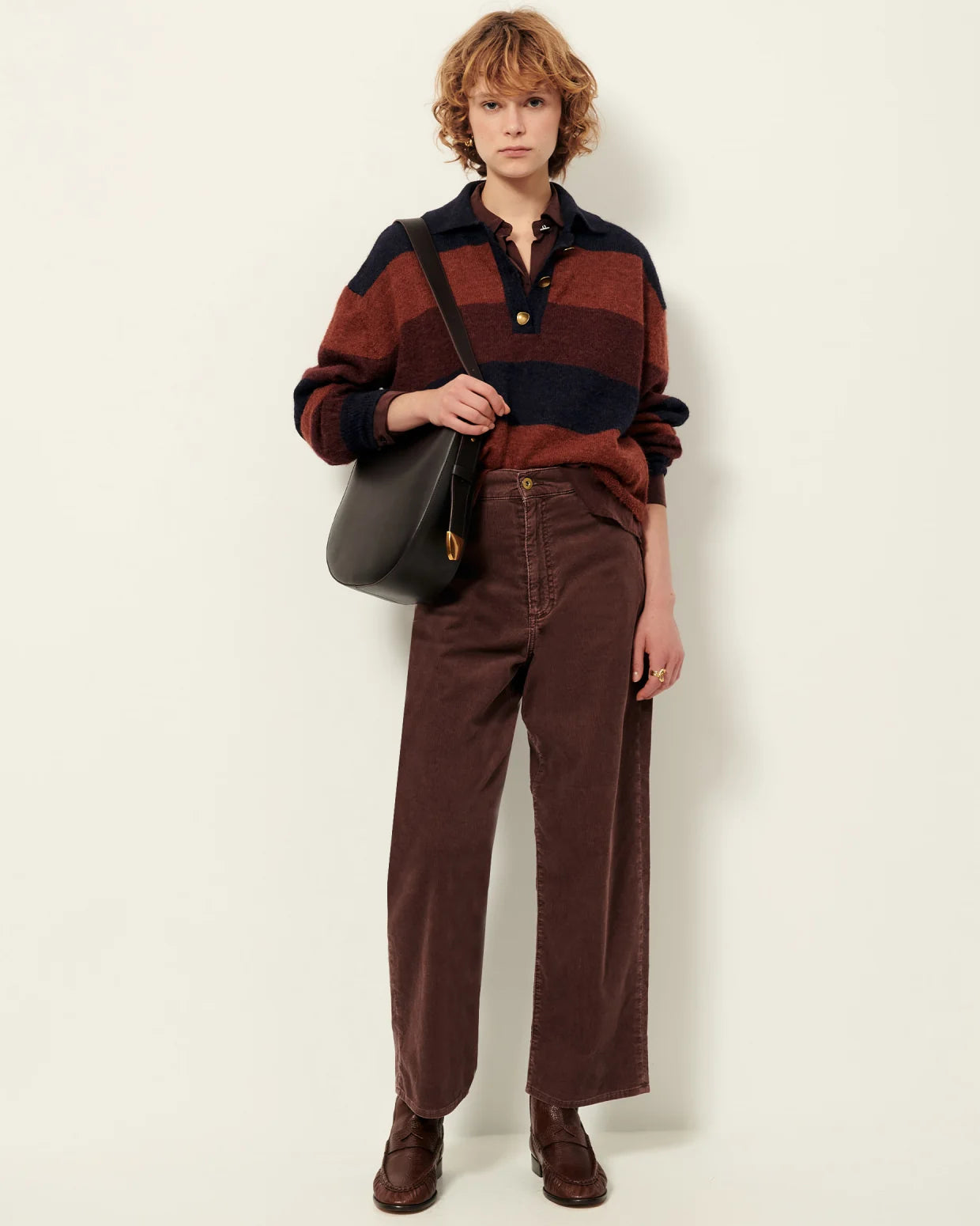 Person wearing a striped sweater and brown pants holding a black bag against a white background