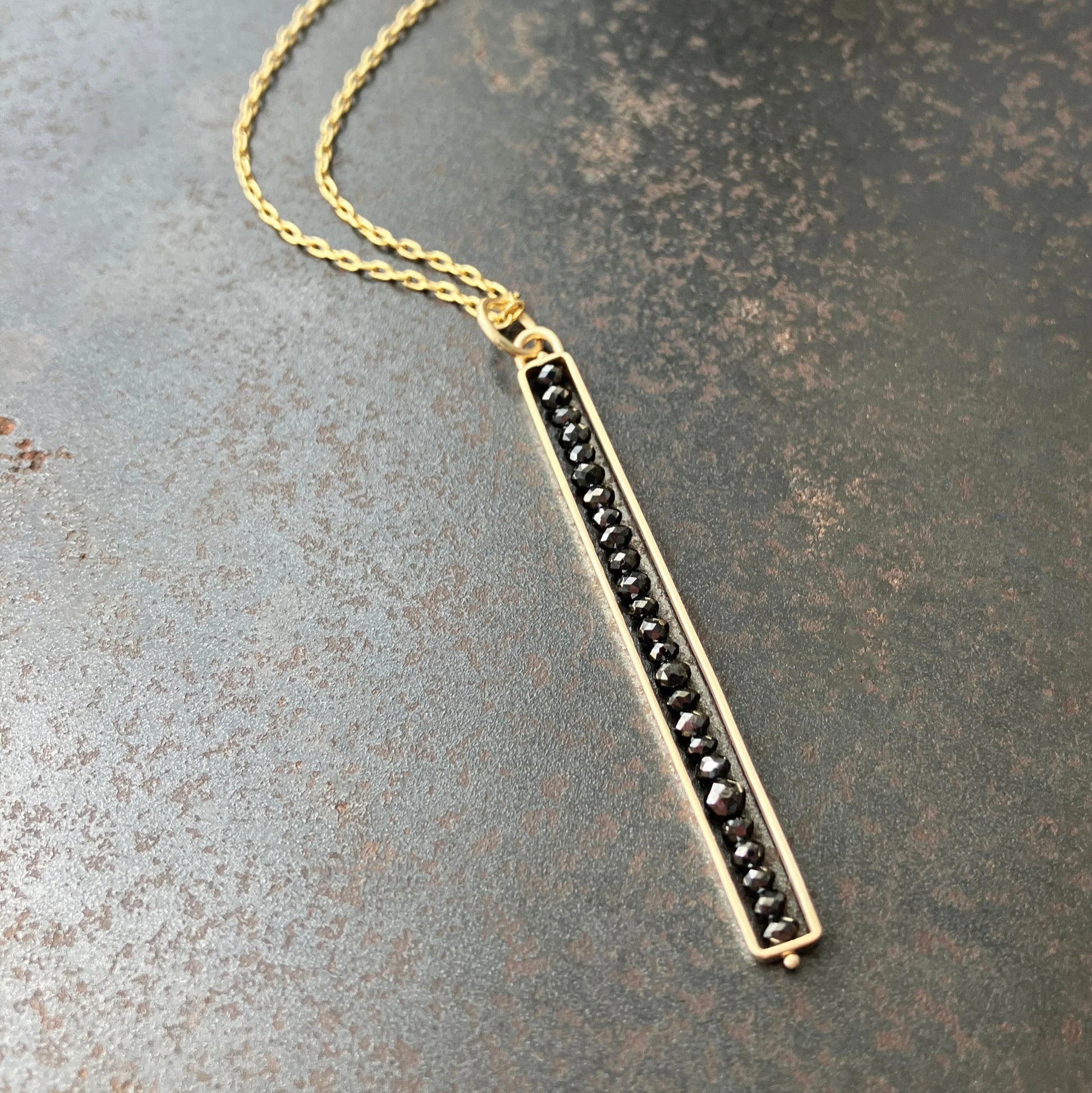 Gold necklace with black beads on a textured surface