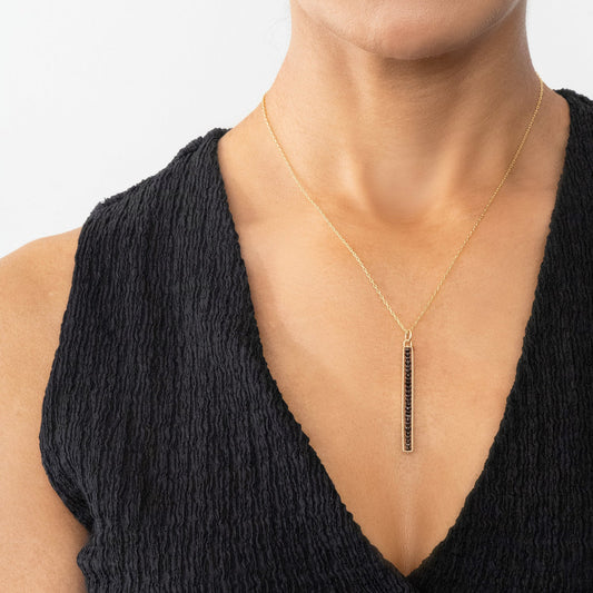 Gold necklace with a pendant on a person wearing a black top against a white background