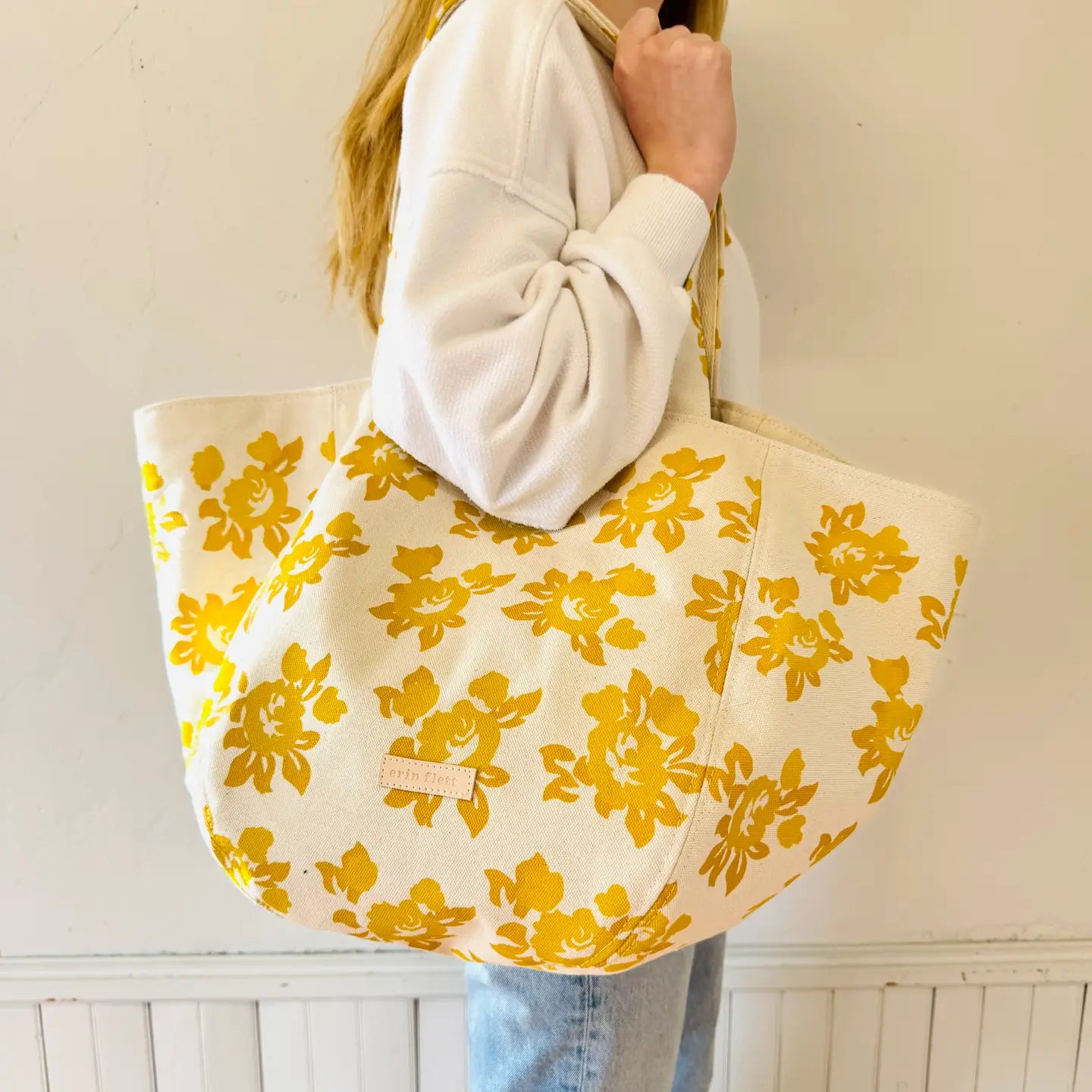 Person holding a yellow floral tote bag against a white background