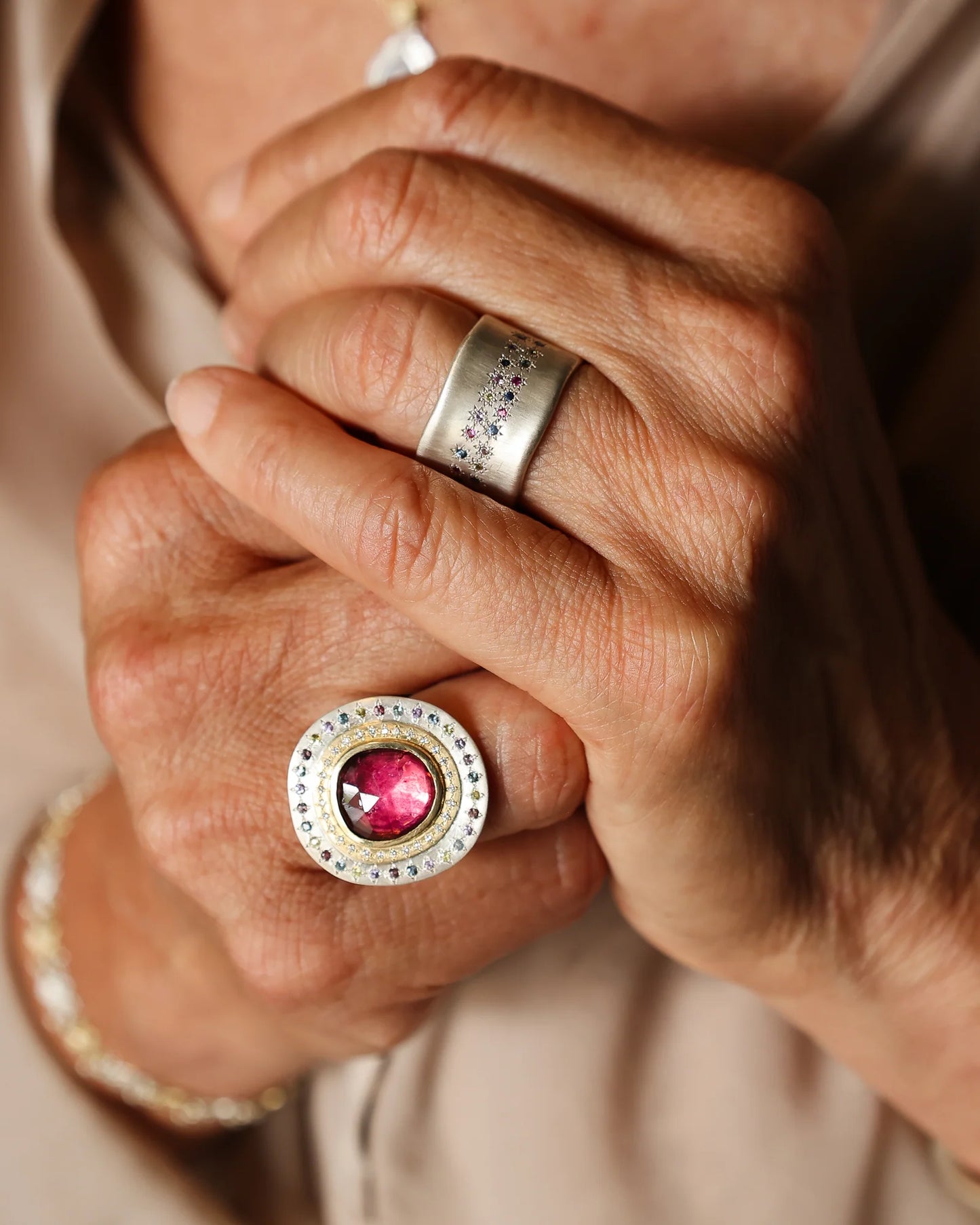 Close-up of hands wearing two rings with gemstones, one pink and one silver.