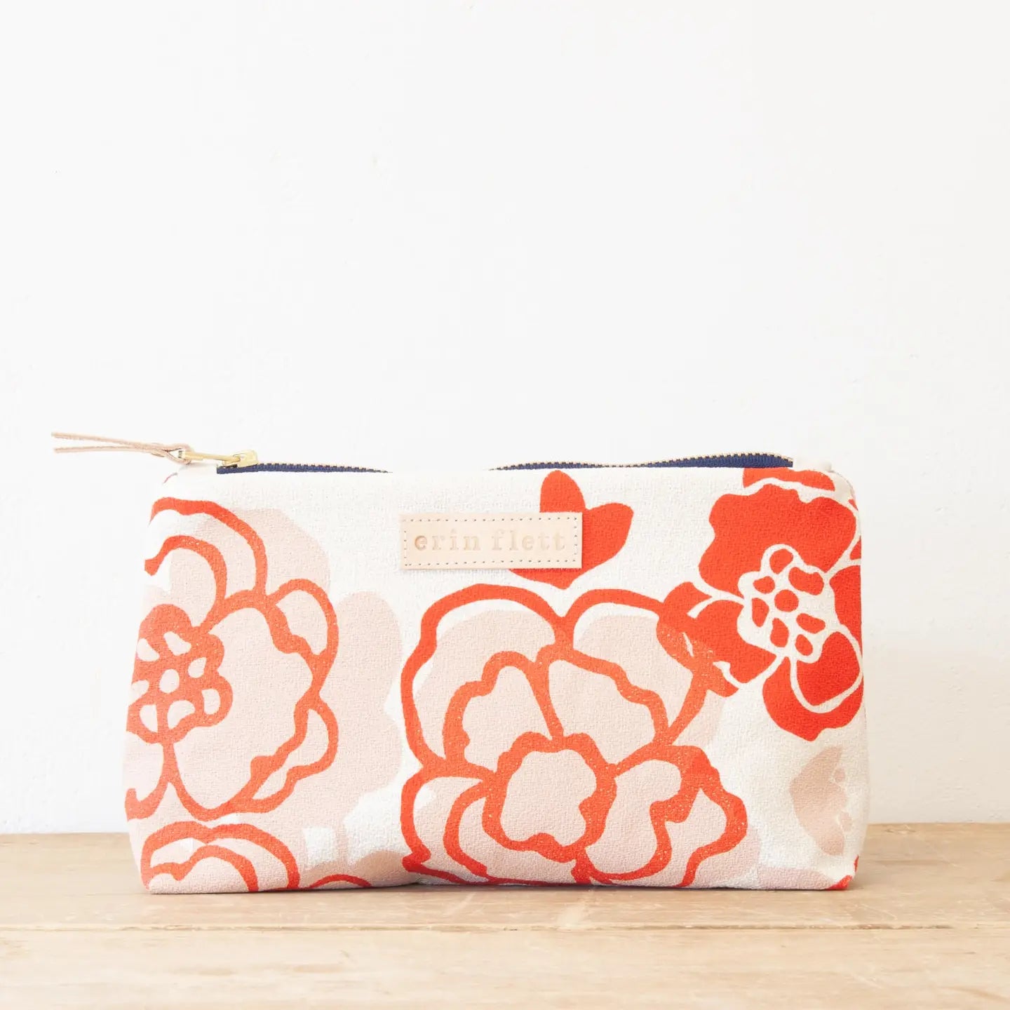 Floral patterned pouch with a visible brand label on a wooden surface.