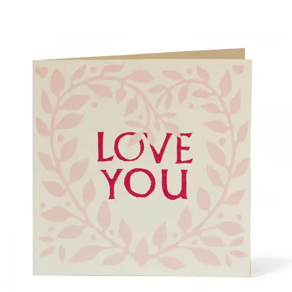 Greeting card with pink heart shaped wreath illustration and Love You written in the middle of the heart in bright pink