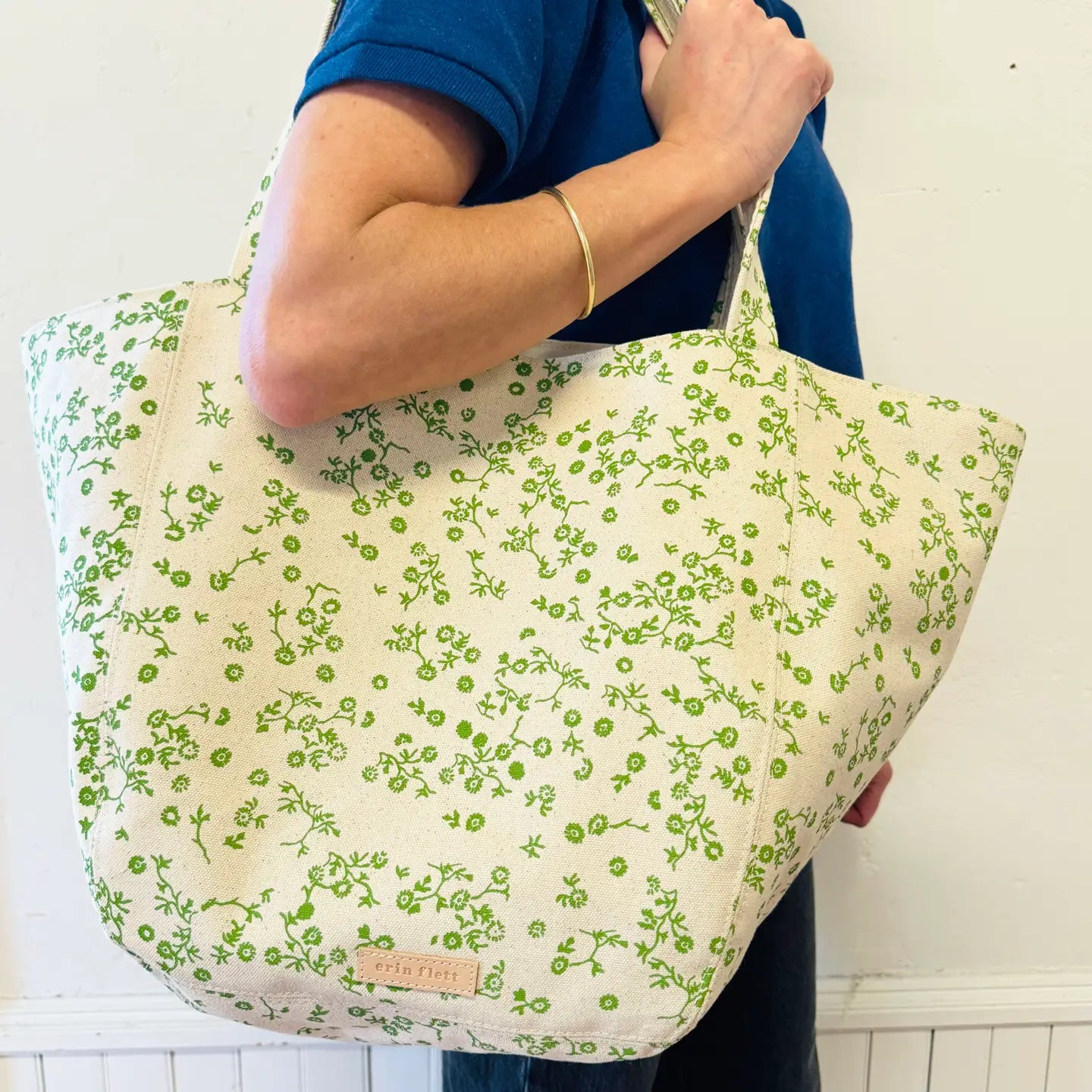 Person holding a green floral-patterned bag against a white background