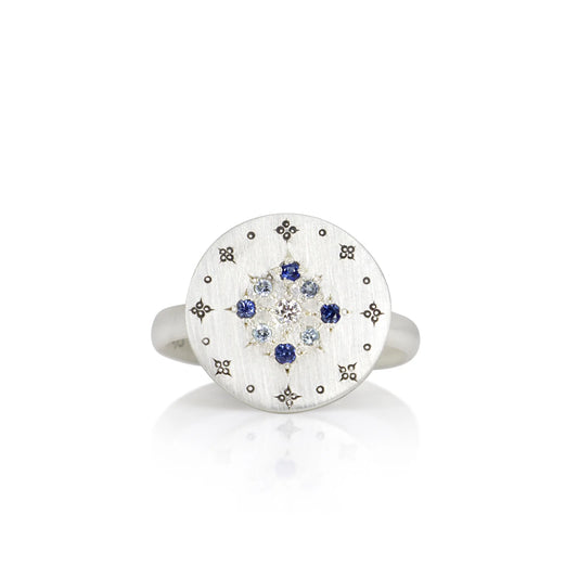 Silver ring with a circular design featuring blue stones on a white background