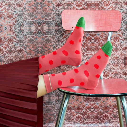 Person wearing strawberry-themed socks sitting on a chair with a patterned floor.