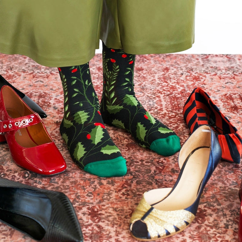 Person wearing green patterned socks with red shoes and colorful flats on a textured floor.