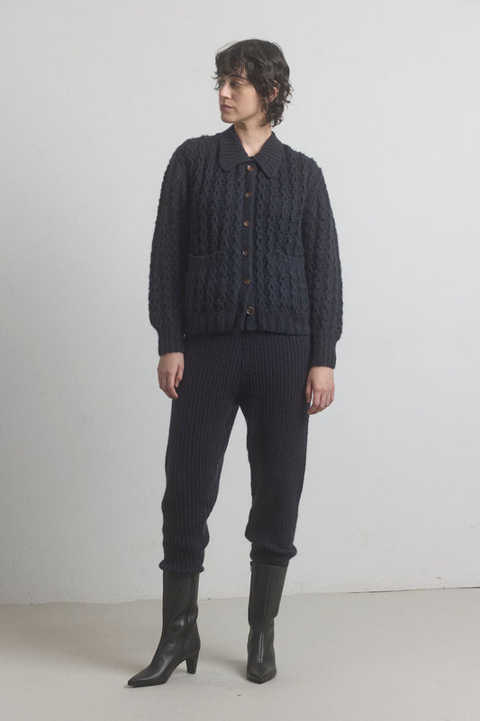 A person standing wearing merino cashmere ribbed joggers with a drawstring waistband, in a dark color, paired with a button-up shirt and boots.