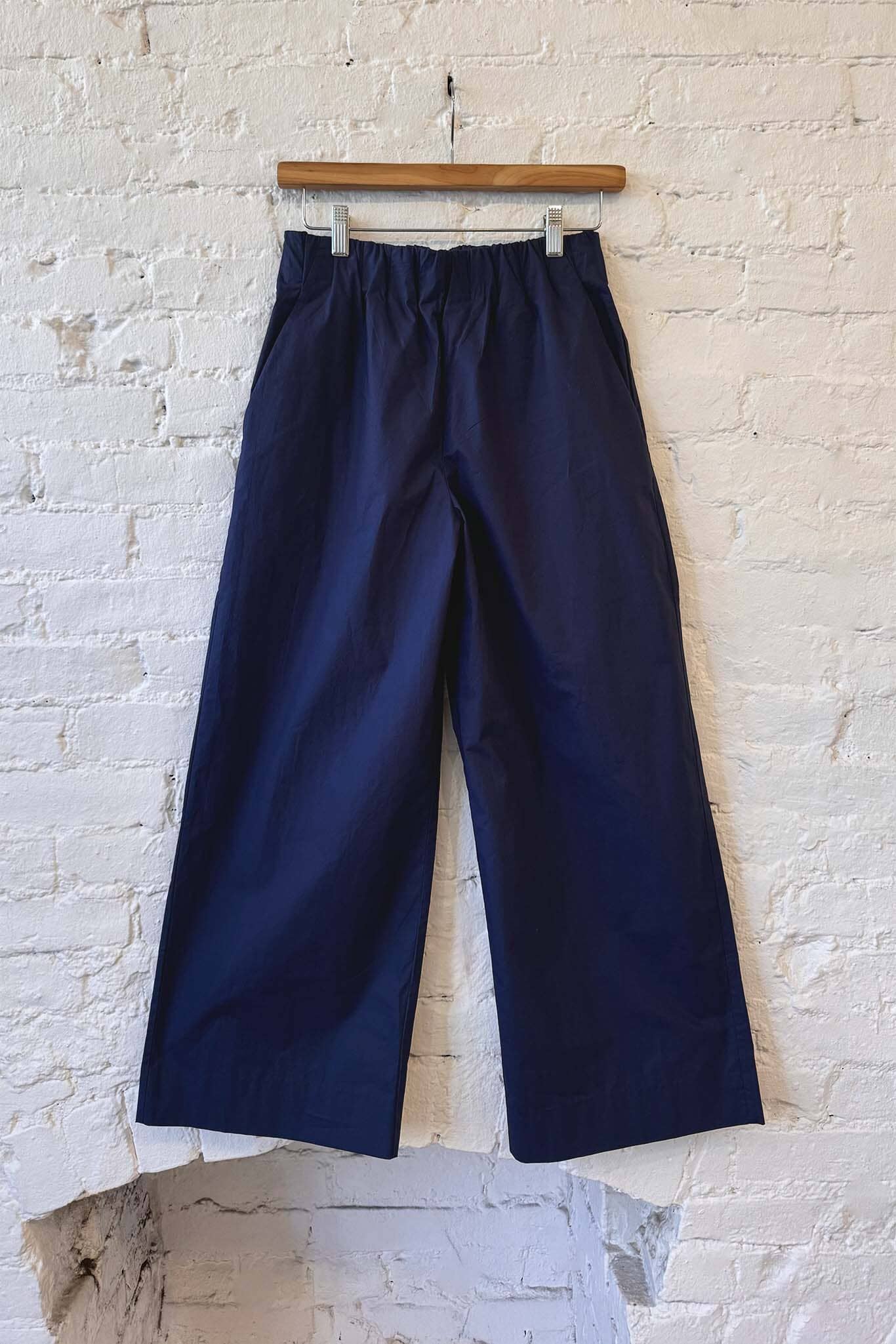 Navy blue pants hanging against a textured white brick wall.