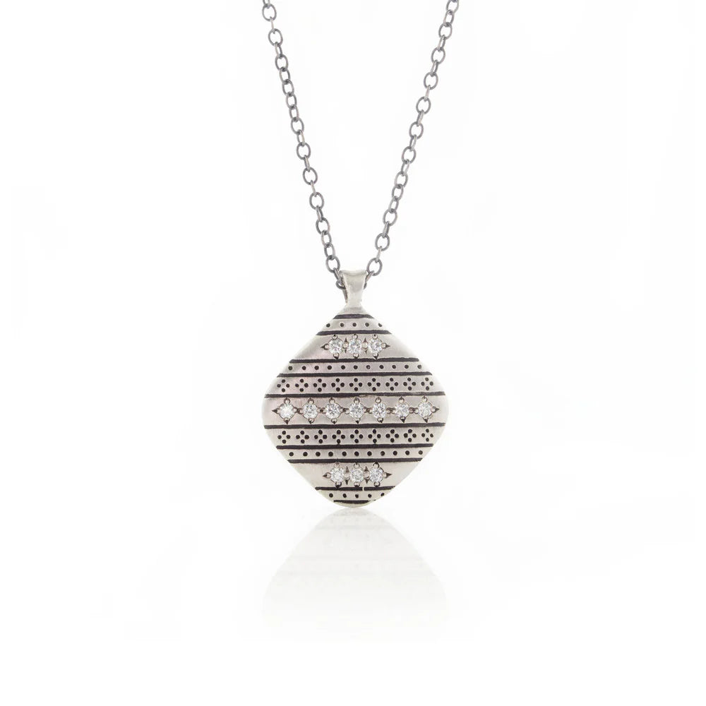 Silver necklace with a round, patterned pendant on a white background