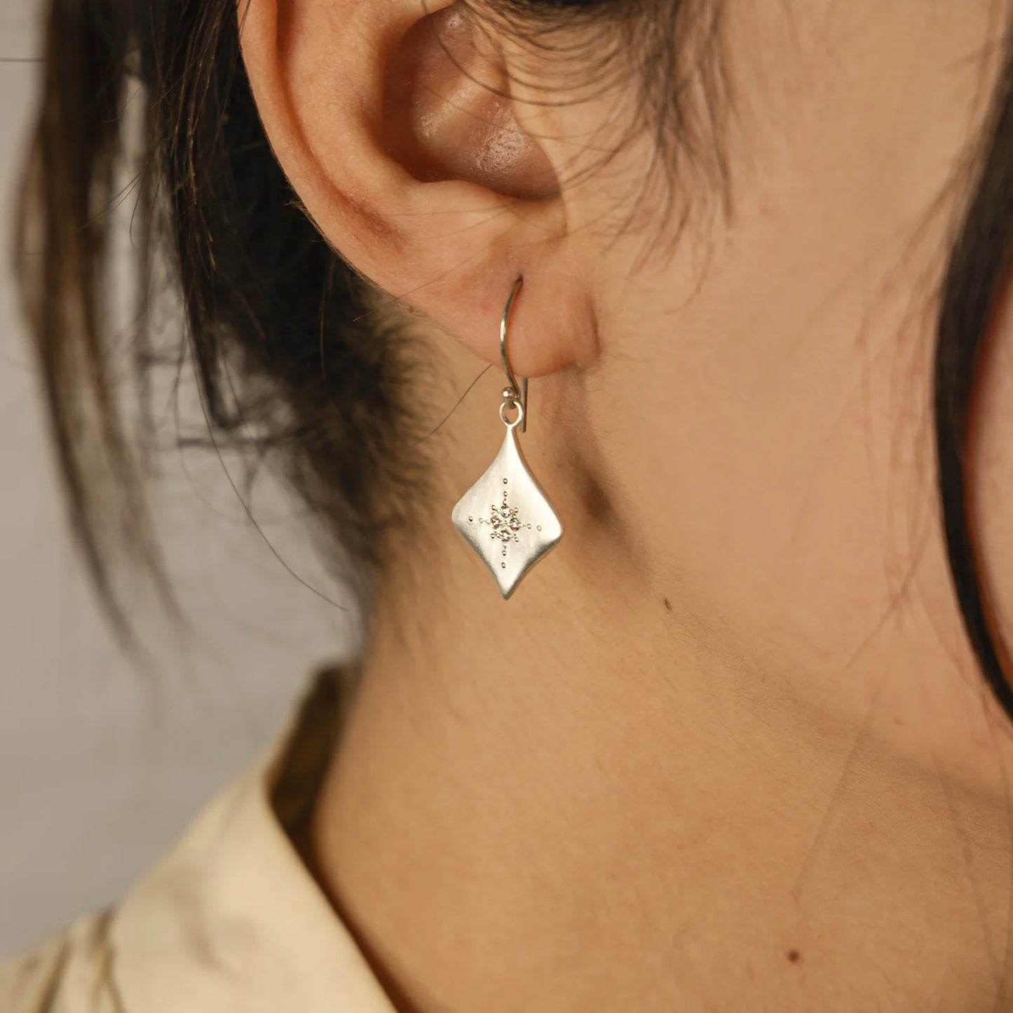 Close-up of a person wearing a silver earring with a geometric design.