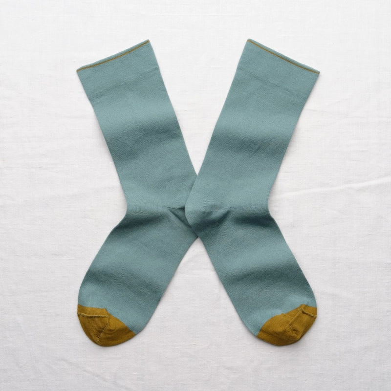 Pair of light blue socks with mustard yellow toes and cuffs on a white background