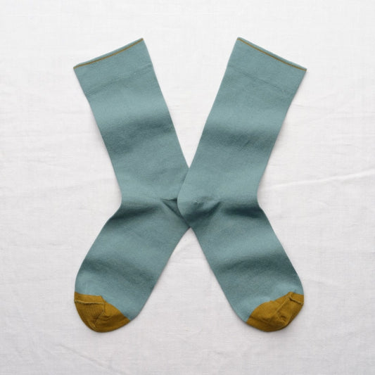 Pair of light blue socks with mustard yellow toes and cuffs on a white background