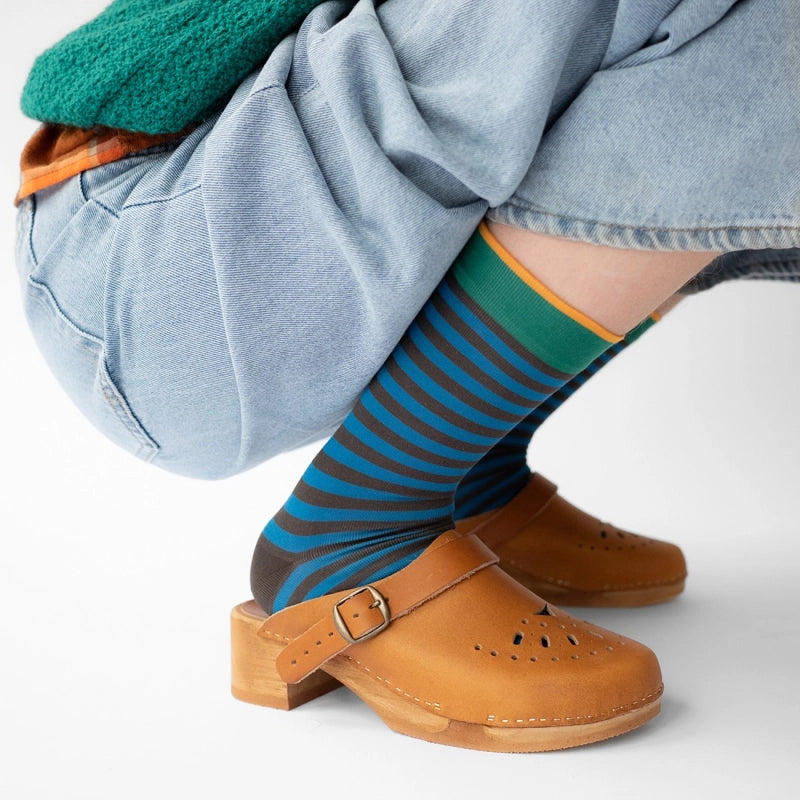 Person wearing blue striped socks with brown clogs on a white background