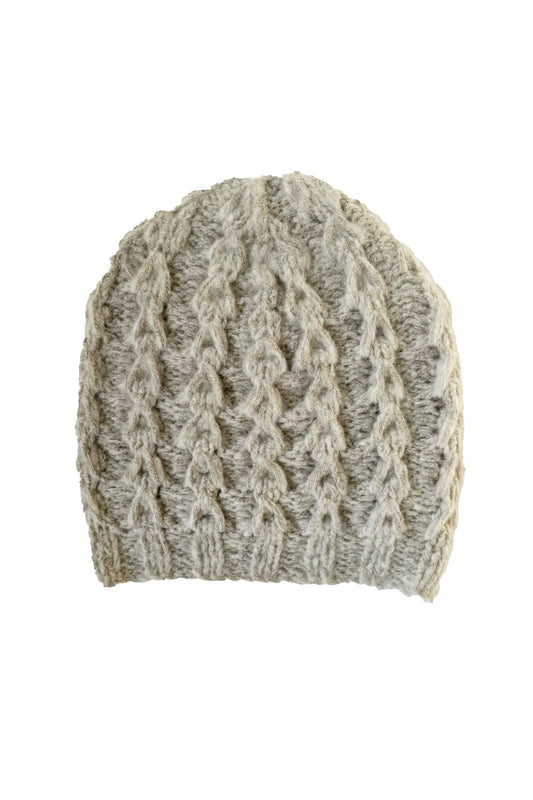 A beige, hand knit merino cashmere beanie with a ribbed hem and cable knit pattern.